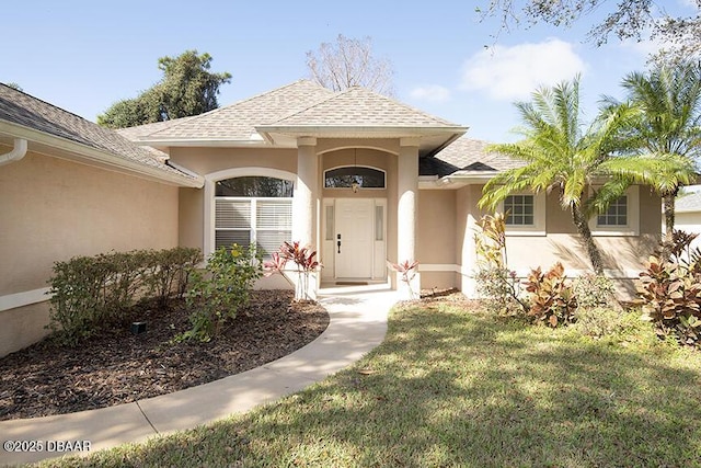 property entrance with roof with shingles, a yard, and stucco siding