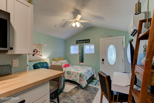 bedroom with ceiling fan, vaulted ceiling, and a textured ceiling