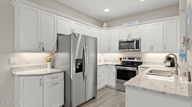 kitchen featuring sink, appliances with stainless steel finishes, white cabinetry, light stone countertops, and light hardwood / wood-style floors