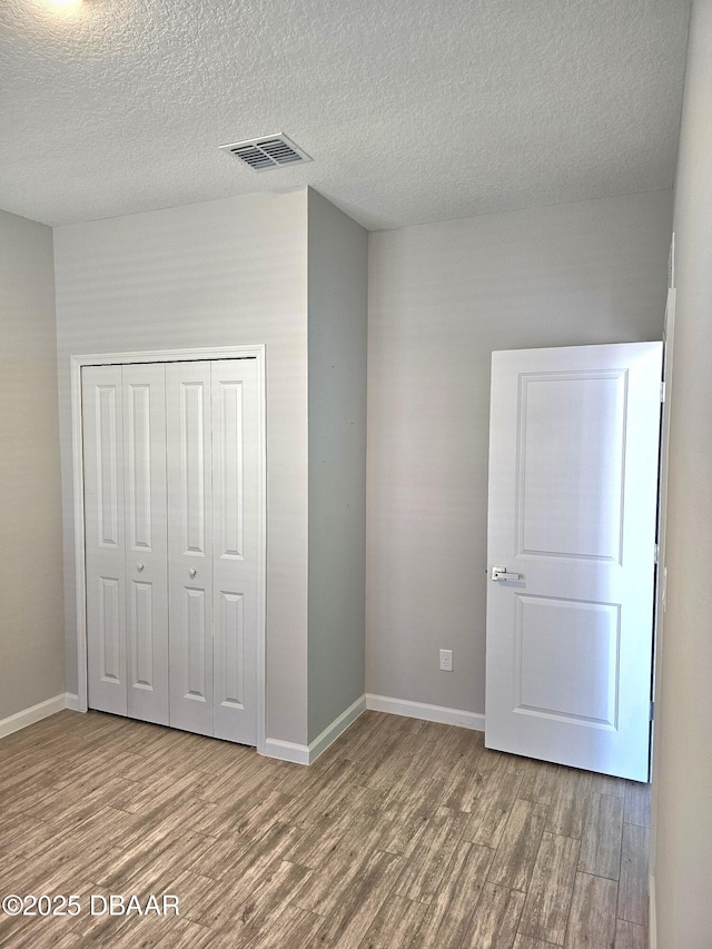 unfurnished bedroom featuring baseboards, a closet, visible vents, and wood finished floors