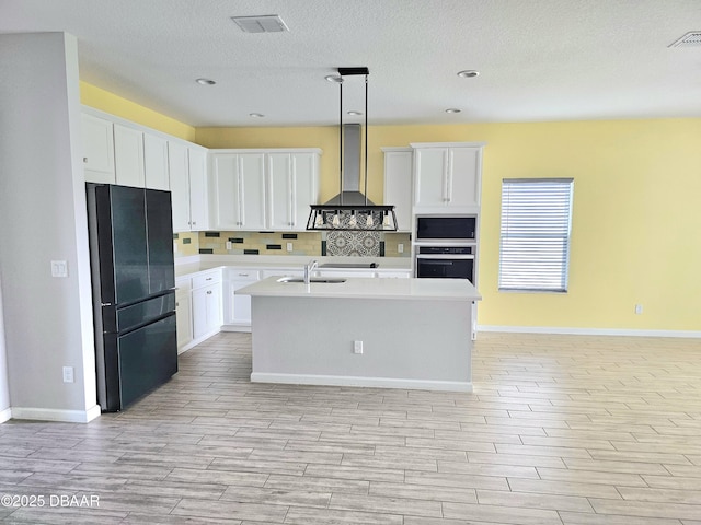 kitchen with light countertops, freestanding refrigerator, wall chimney range hood, built in microwave, and oven