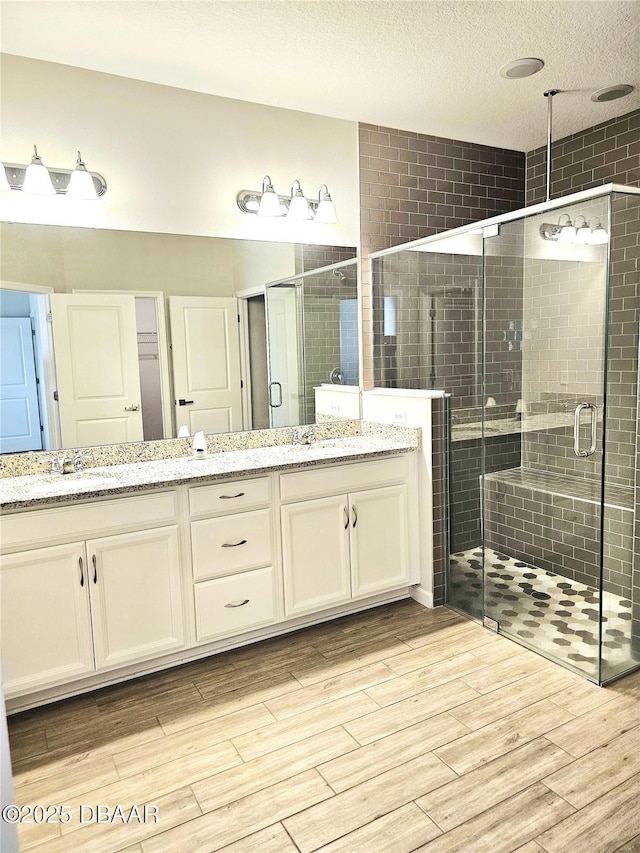 bathroom featuring double vanity, wood finished floors, a textured ceiling, a shower stall, and a sink