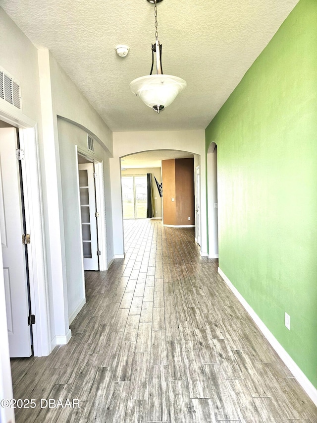 hallway with baseboards, visible vents, arched walkways, wood finished floors, and a textured ceiling