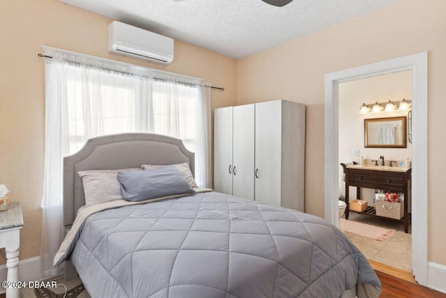 bedroom featuring a wall mounted AC, a textured ceiling, sink, hardwood / wood-style flooring, and ensuite bathroom