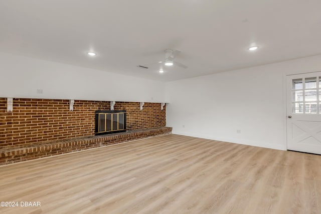 unfurnished living room featuring a brick fireplace, ceiling fan, brick wall, and light hardwood / wood-style flooring