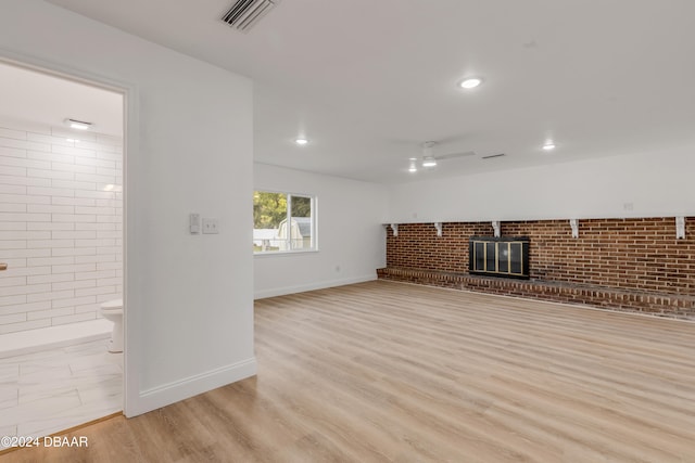 unfurnished living room featuring brick wall, ceiling fan, and light hardwood / wood-style flooring