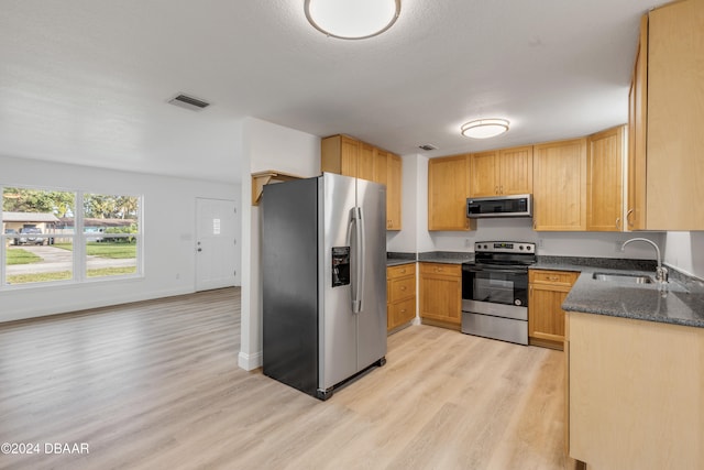 kitchen featuring stainless steel appliances, dark stone counters, a textured ceiling, sink, and light wood-type flooring