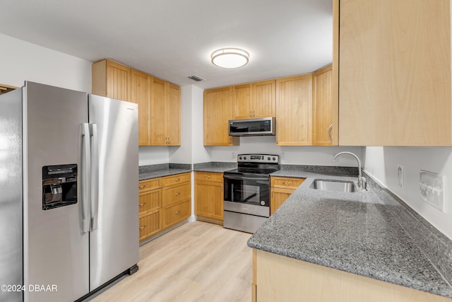 kitchen featuring stainless steel appliances, dark stone counters, sink, and light hardwood / wood-style flooring