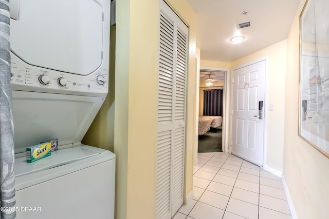 laundry area with visible vents, stacked washing maching and dryer, light tile patterned floors, baseboards, and laundry area