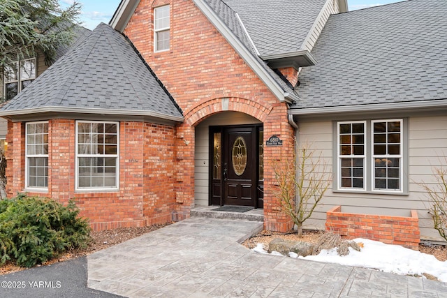 property entrance featuring brick siding and roof with shingles