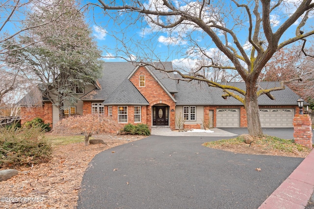 view of front facade featuring a garage, driveway, brick siding, and a shingled roof