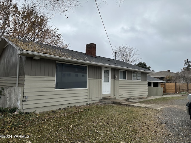 rear view of house featuring entry steps, a yard, a chimney, and fence