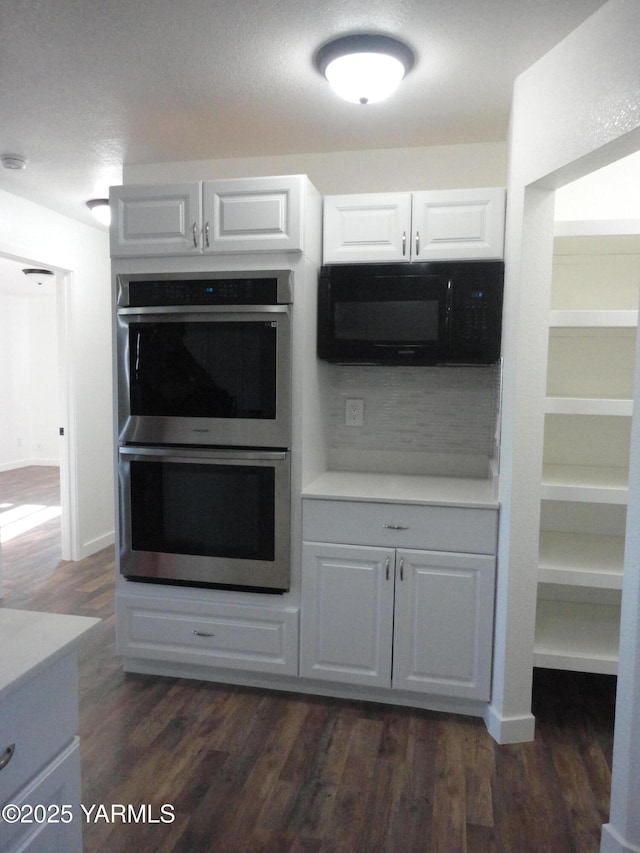 kitchen featuring stainless steel double oven, dark wood finished floors, light countertops, black microwave, and white cabinetry