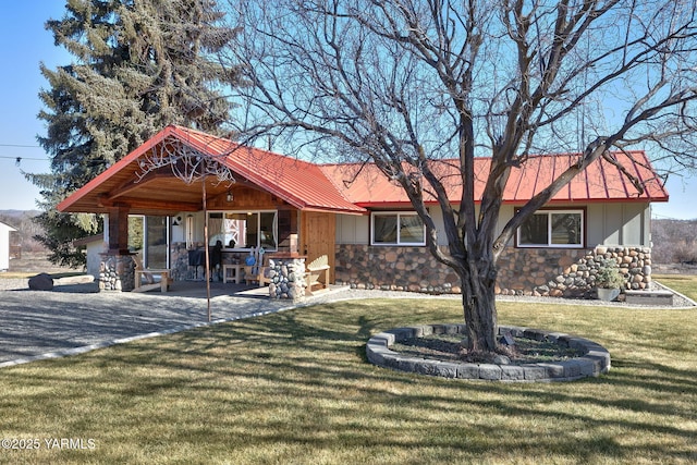 view of front of home with stone siding, a patio, a front lawn, and metal roof