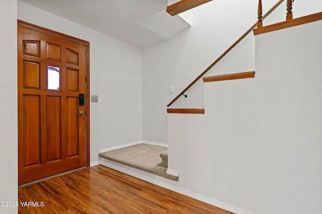 foyer featuring baseboards, wood finished floors, and stairway