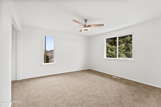 carpeted spare room featuring baseboards, visible vents, and ceiling fan