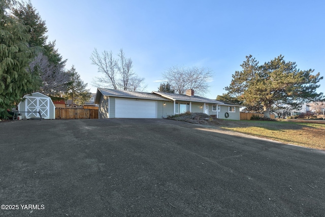 single story home with aphalt driveway, a storage shed, a front yard, fence, and a garage