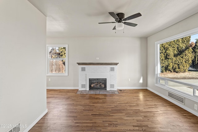 unfurnished living room featuring a brick fireplace, baseboards, visible vents, and wood finished floors