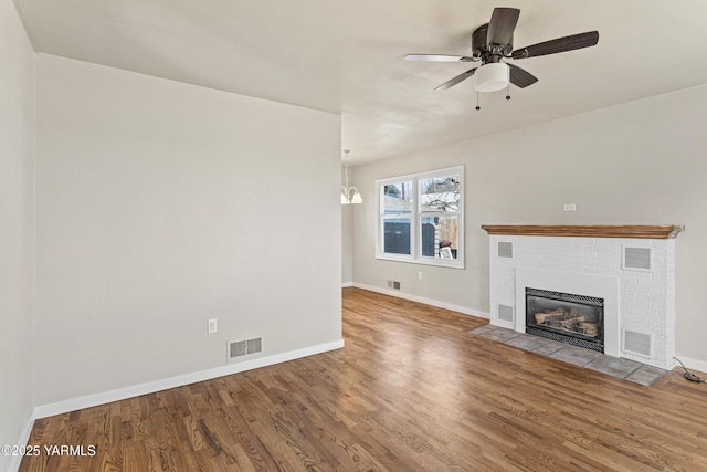 unfurnished living room featuring a brick fireplace, wood finished floors, and visible vents