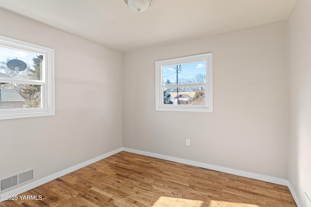 unfurnished room with baseboards, visible vents, a wealth of natural light, and wood finished floors