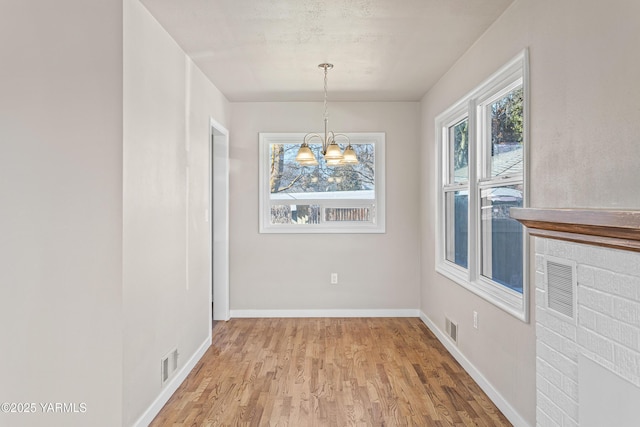 unfurnished dining area with a notable chandelier, wood finished floors, visible vents, and baseboards