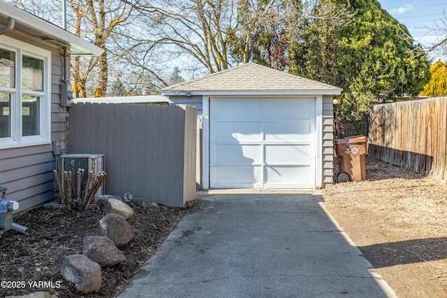 detached garage with driveway, central air condition unit, and fence