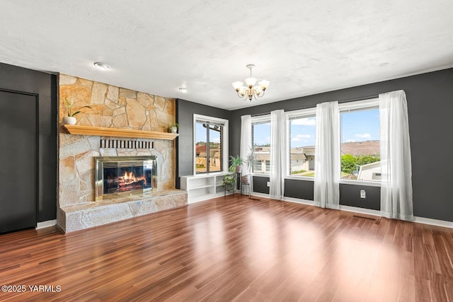 unfurnished living room featuring a stone fireplace, visible vents, wood finished floors, baseboards, and an inviting chandelier