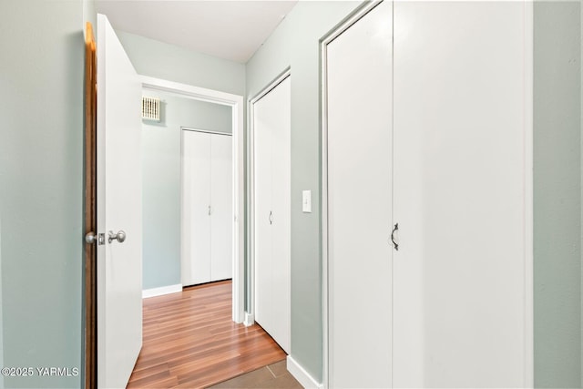 hall featuring baseboards, visible vents, and wood finished floors