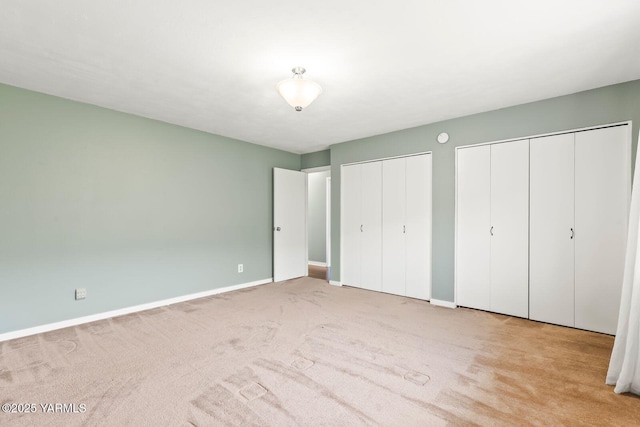 unfurnished bedroom featuring carpet floors, baseboards, and two closets