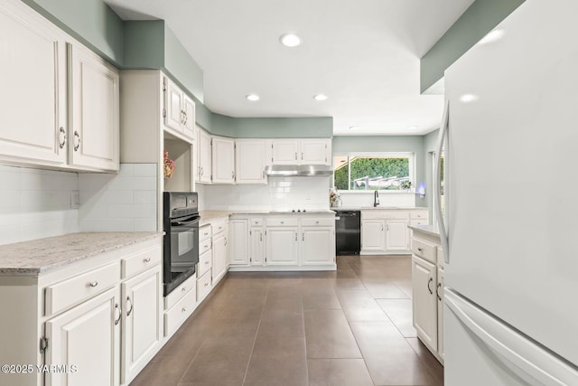 kitchen with white cabinets, tasteful backsplash, under cabinet range hood, dark tile patterned floors, and black appliances
