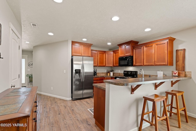 212 Golding St, Moxee, WA 98936 - kitchen featuring black appliances, a peninsula, brown cabinets, light wood finished floors, and recessed lighting
