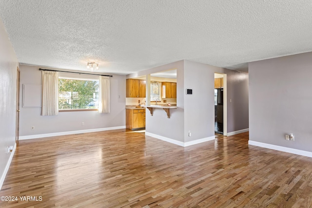 unfurnished living room featuring a textured ceiling, light wood finished floors, a sink, and baseboards