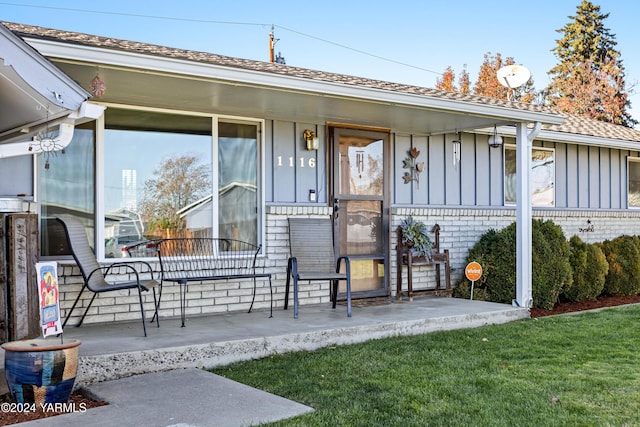 entrance to property featuring board and batten siding, covered porch, brick siding, and a lawn