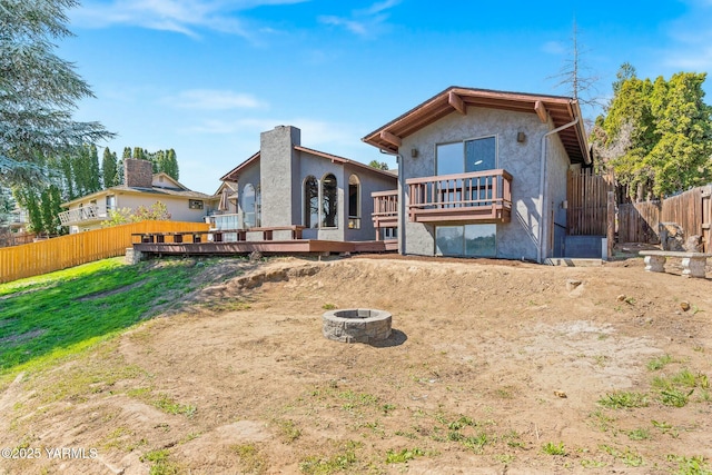 back of house featuring a fire pit, a wooden deck, fence, and stucco siding