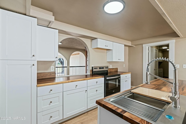 kitchen with stainless steel electric range oven, light wood-style flooring, wooden counters, and white cabinetry