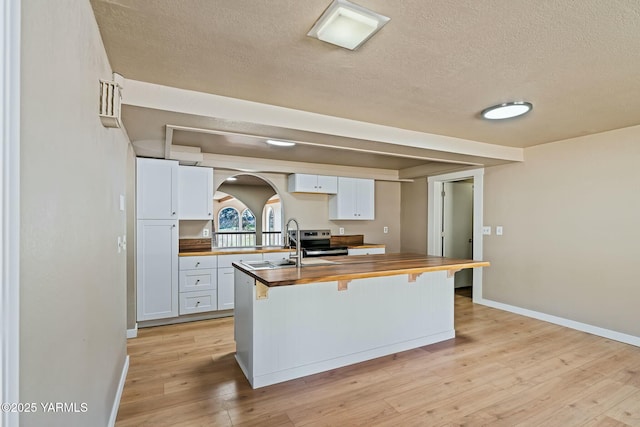 kitchen featuring wood counters, light wood-style flooring, a textured ceiling, a breakfast bar area, and white cabinetry