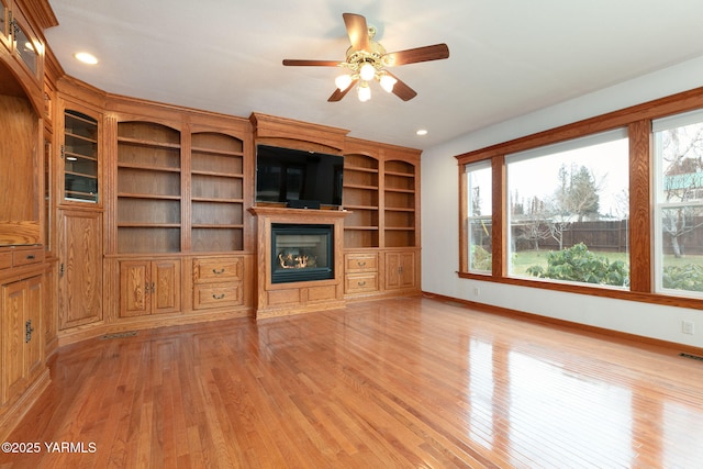 unfurnished living room with a glass covered fireplace, light wood-style floors, baseboards, and recessed lighting