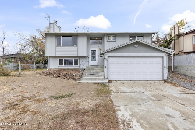 split foyer home featuring a garage, a chimney, fence, and driveway