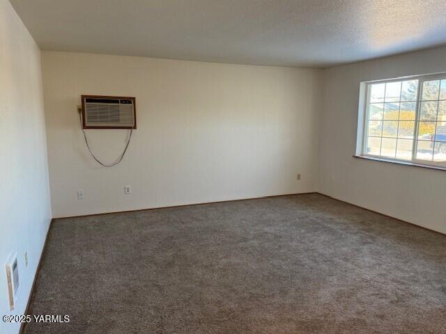 carpeted spare room featuring visible vents, a textured ceiling, and a wall mounted AC