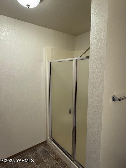 bathroom featuring tile patterned floors, baseboards, a stall shower, and a textured wall