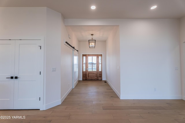 entryway with baseboards, light wood finished floors, a barn door, and recessed lighting