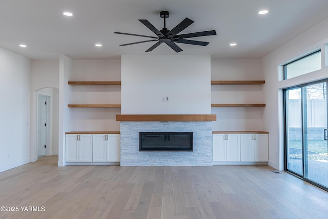 unfurnished living room with arched walkways, a fireplace, recessed lighting, a ceiling fan, and light wood-type flooring