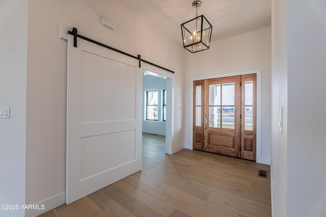 foyer entrance featuring a barn door, light wood-type flooring, visible vents, and baseboards