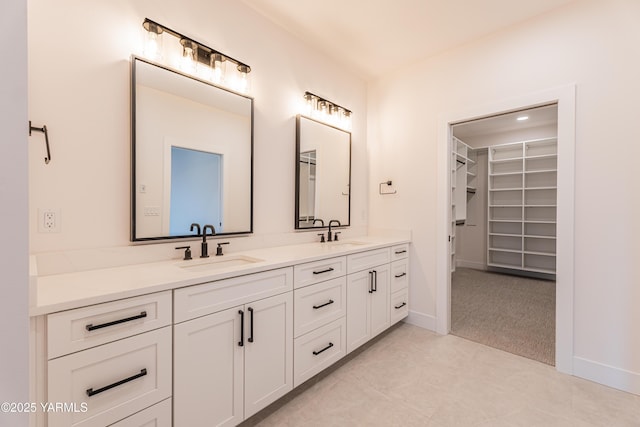 full bathroom featuring double vanity, baseboards, a walk in closet, and a sink