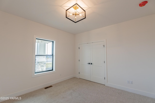 unfurnished room with light carpet, an inviting chandelier, visible vents, and baseboards