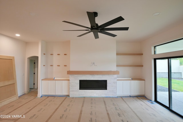 unfurnished living room with arched walkways, a fireplace, recessed lighting, light wood-type flooring, and baseboards