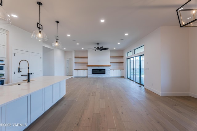 kitchen featuring decorative light fixtures, open floor plan, a sink, light stone countertops, and light wood-type flooring