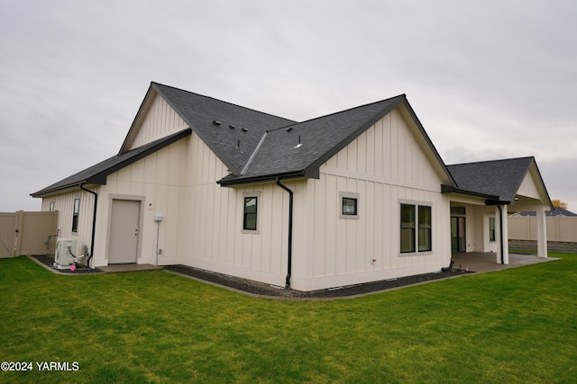 back of property with board and batten siding, a yard, a shingled roof, and fence