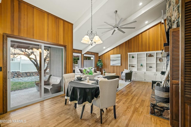 dining space featuring vaulted ceiling with beams, wood walls, light wood finished floors, and a notable chandelier