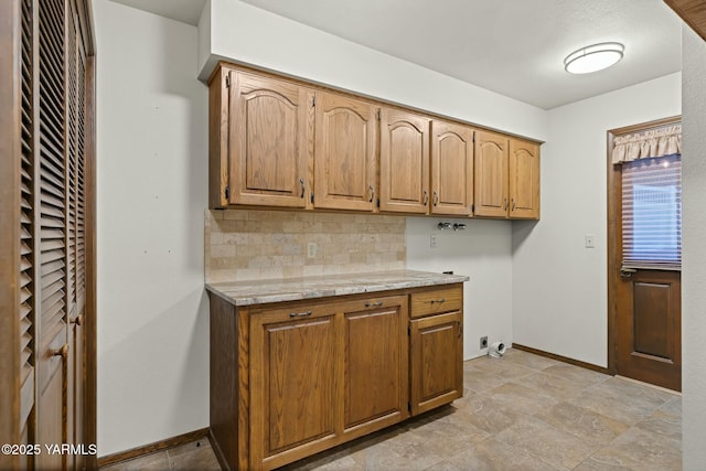 kitchen featuring tasteful backsplash, brown cabinets, baseboards, and light stone countertops